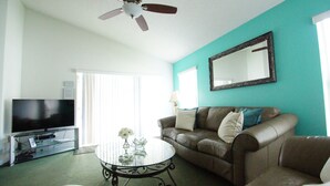 A living room with a television, a glass coffee table, a brown leather sofa, and a ceiling fan. - Amazing villa - Close to Disneyworld (Clermont)