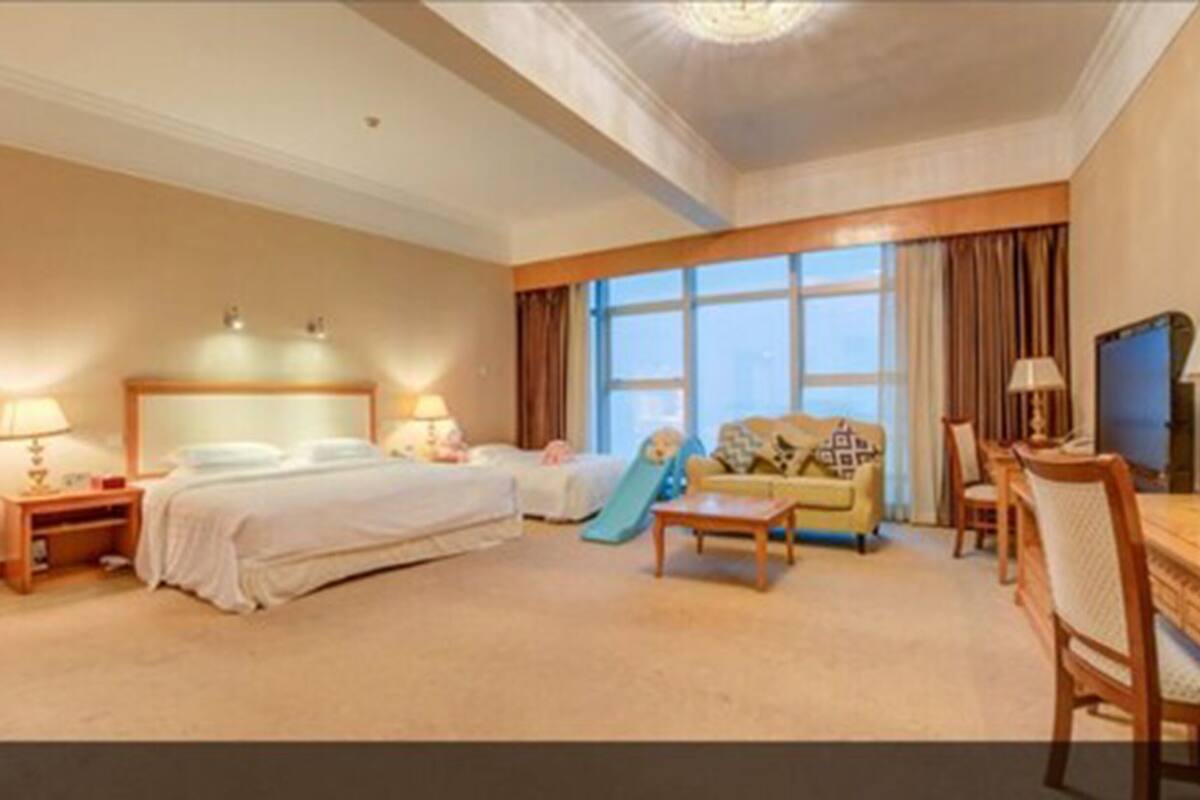 A hotel room with a bed, a desk, a chair, a sofa, a TV, and a window with curtains.