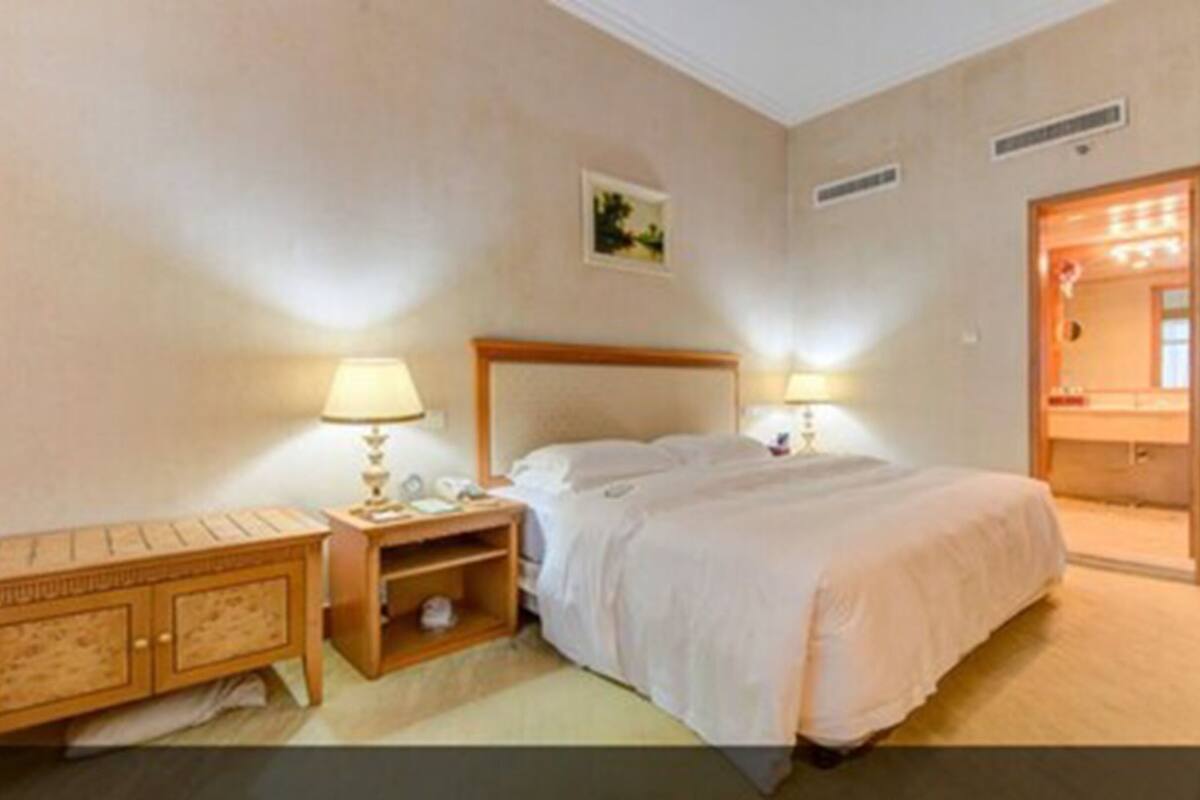 A hotel room with a bed, bedside tables, a nightstand, a mirror, and a door leading to a bathroom.