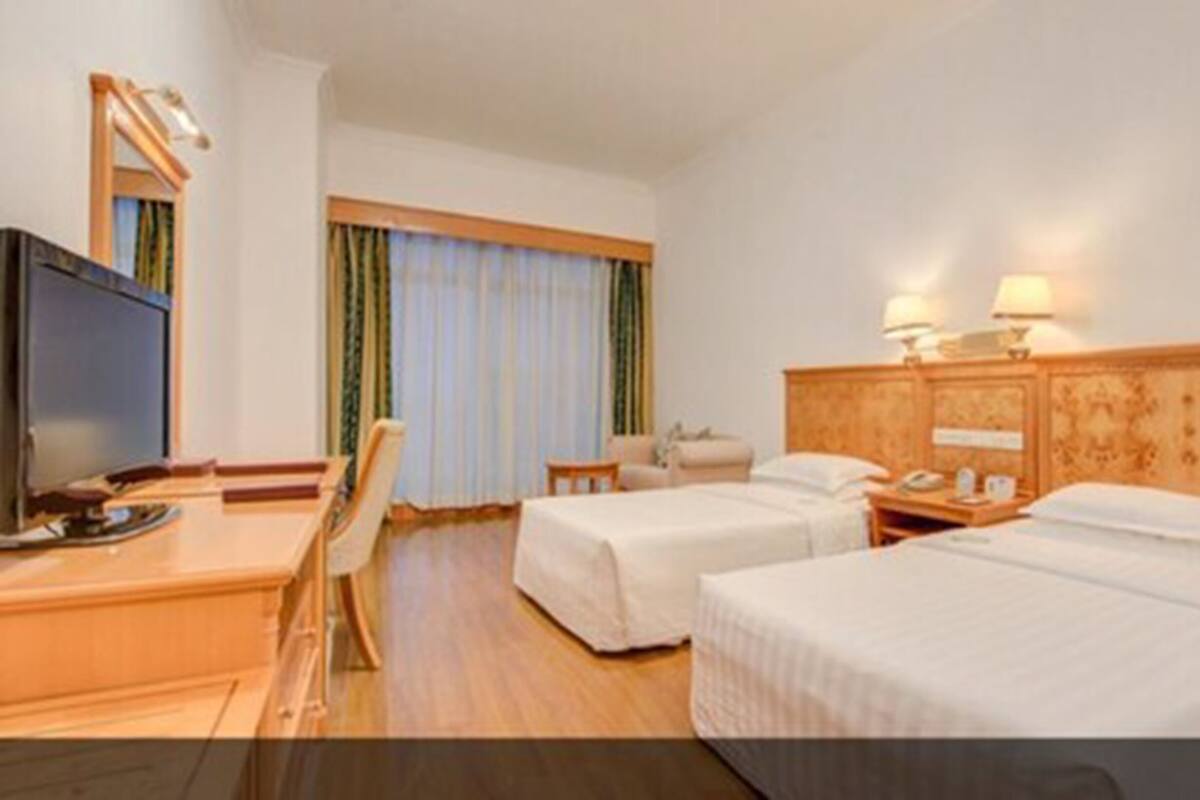 A hotel room with two single beds, a desk with a television, a chair, and a window with curtains.