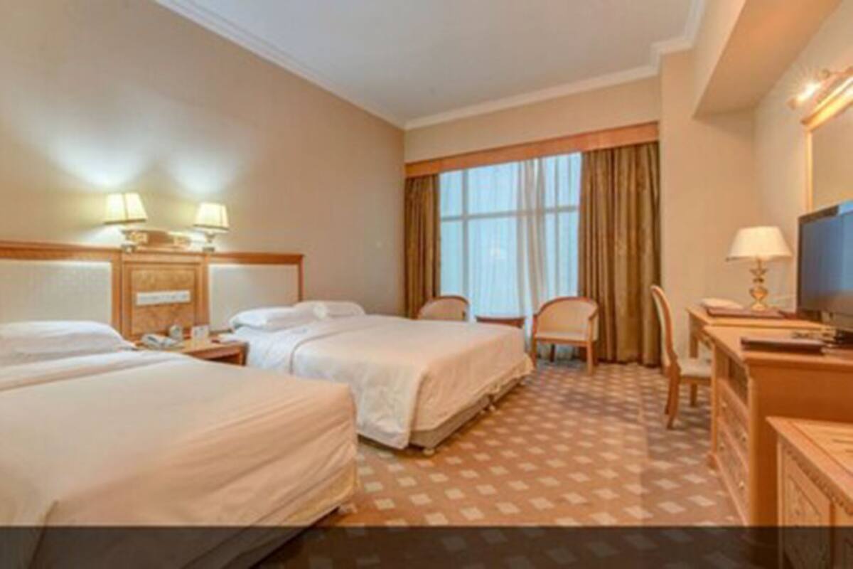 A hotel room with two beds, a desk with a TV, a chair, and a window with curtains.