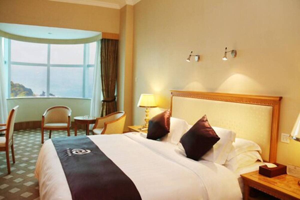 A hotel room with a large bed, two bedside lamps, a desk with a chair, and a window with curtains.
