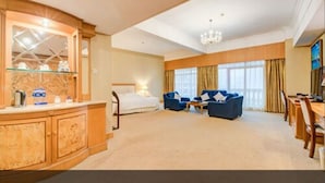 Een ruime hotelkamer met een groot bed, een zithoek met twee banken, een eettafel en een groot raam met gordijnen.