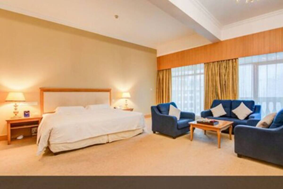 A hotel room with a large bed, two armchairs, a coffee table, and a nightstand with lamps.