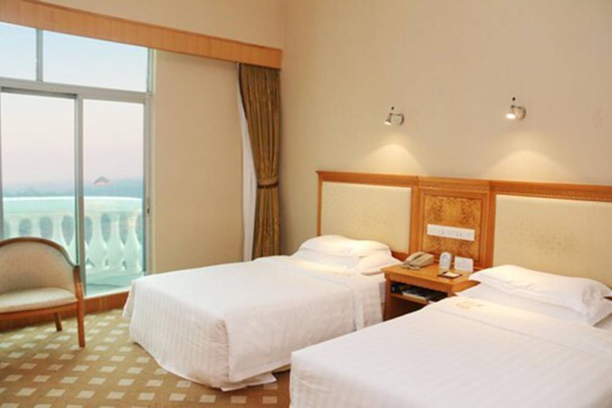 A hotel room with two beds, a chair, a nightstand with a phone, and a view of the sea through a large window.