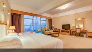 Een hotelkamer met een groot bed, een televisie, een bureau en uitzicht op de stad.