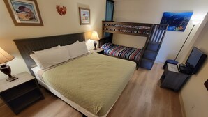 Un dormitorio con una cama grande, una mesita de noche con lámpara, una cama litera y un cuadro en la pared.
