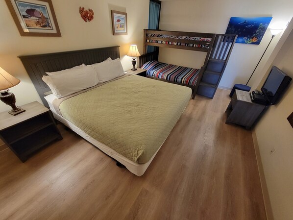 A bedroom with a large bed, a nightstand with a lamp, a bunk bed, and a painting on the wall.