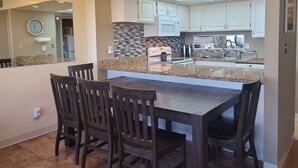 Una cocina moderna con armarios blancos, encimera de granito y comedor con sillas de madera oscura.