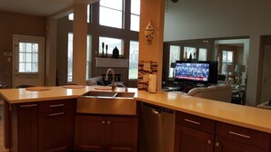 A modern kitchen with a built-in dishwasher, a sink, and a countertop. There is a television displaying a news broadcast. -  The Oasis  w/Private Pool & Spa (Houston)
