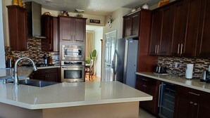 A modern kitchen with dark wooden cabinets, stainless steel appliances, and a large island with stools. -  The Oasis  w/Private Pool & Spa (Houston)