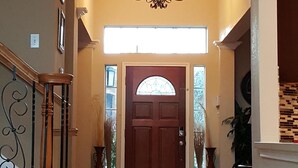 A spacious hallway with a wooden staircase, a chandelier, and a door with a glass window. -  The Oasis  w/Private Pool & Spa (Houston)