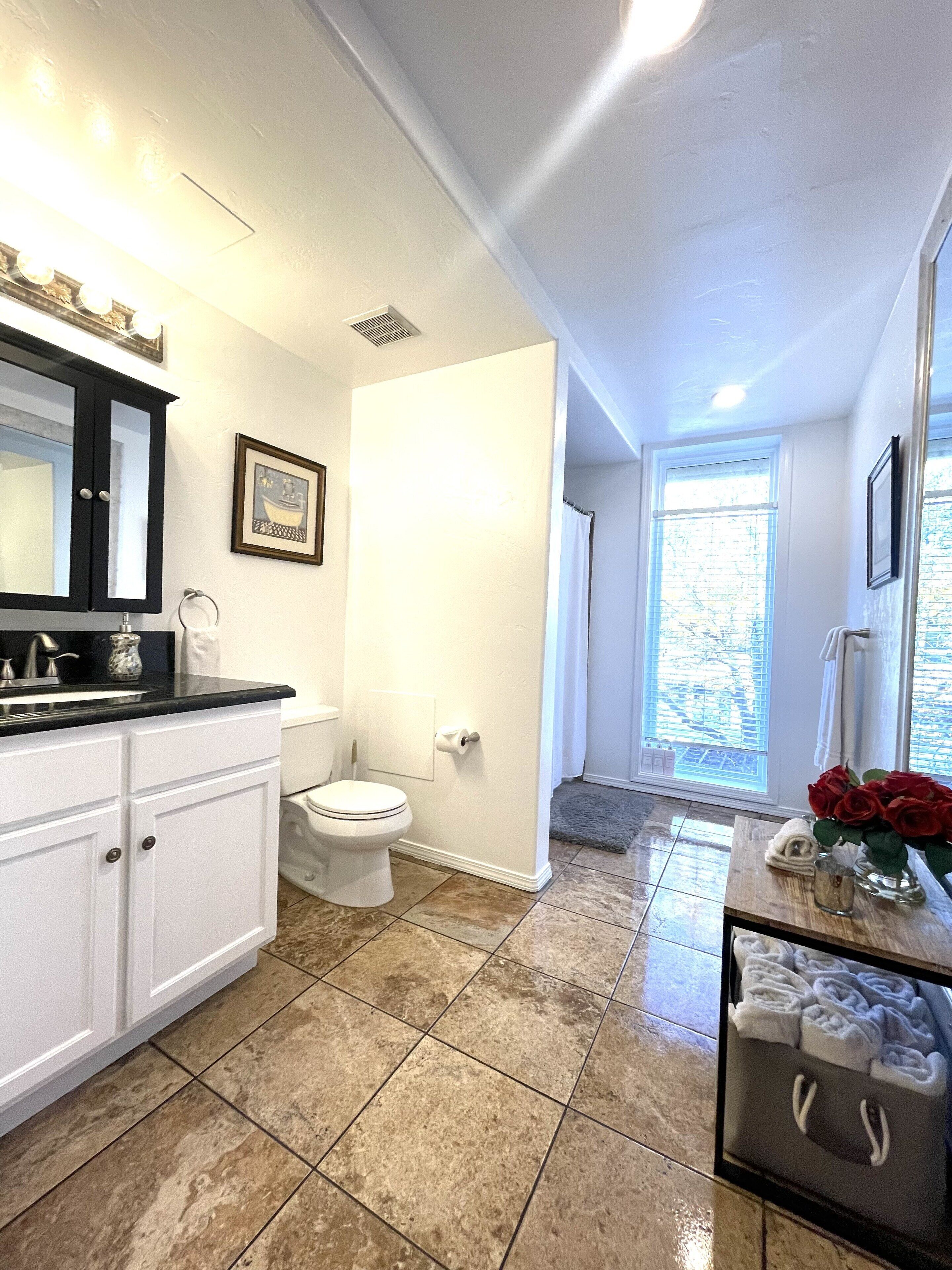 A bathroom with a toilet, sink, and vanity. There is a window providing natural light and a shower area.