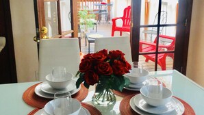 A dining area with a table set for two, a vase with red roses, and a view of an outdoor patio with red chairs and a wooden pergola. - Downtown Suite in Cap Hill ! (Denver)