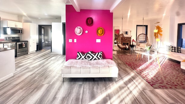 A modern living space with a vibrant pink accent wall, a white sofa, and a kitchen area with stainless steel appliances. - Downtown Suite in Cap Hill ! (Denver)