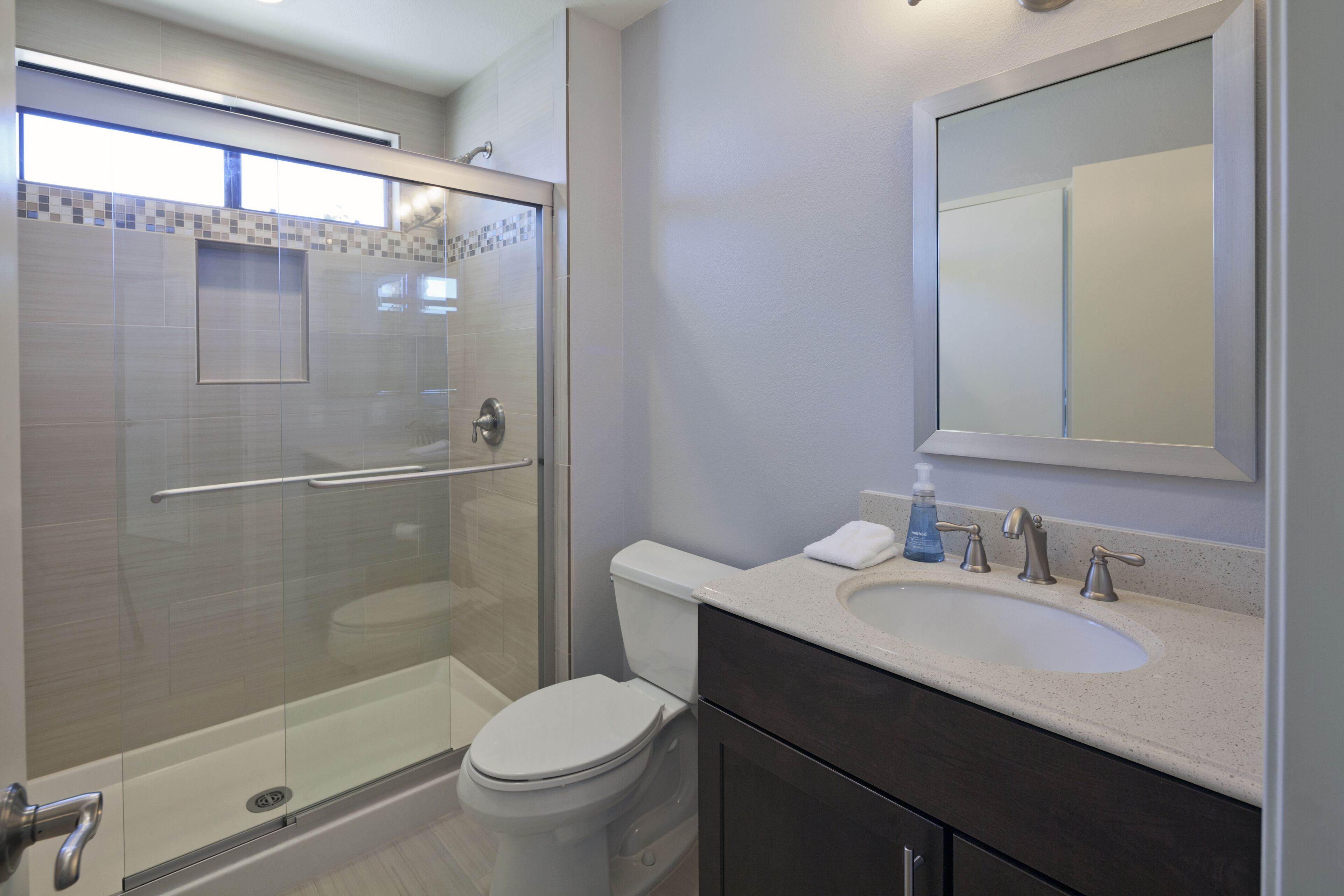 A modern bathroom with a glass-enclosed shower, a toilet, a sink with a mirror above it, and a towel on the counter.