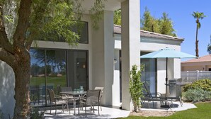 Et moderne hus med en patio, der indeholder et bord, stole, grill og en stor parasol.