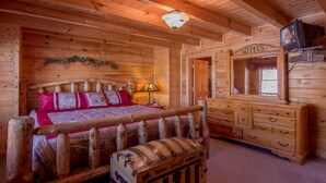 A wooden cabin bedroom with a bed, dresser, and a television. - New Arcade 2-Pools 1 Pool YR RD ,Hot Tub,Mini Golf,FREE WIFI,Game Room (Pigeon Forge)
