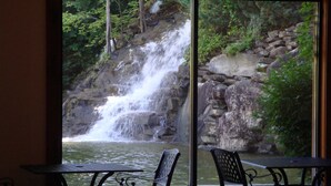 A view of a waterfall through a window, with two metal chairs and a table in the foreground. - New Arcade 2-Pools 1 Pool YR RD ,Hot Tub,Mini Golf,FREE WIFI,Game Room (Pigeon Forge)