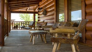 A wooden deck with rustic furniture, including benches and a table, under a covered porch with wooden beams and a railing. - New Arcade 2-Pools 1 Pool YR RD ,Hot Tub,Mini Golf,FREE WIFI,Game Room (Pigeon Forge)