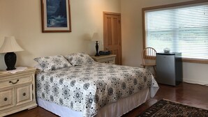Une chambre à coucher comprenant un lit, deux tables de chevet, une commode, une chaise, une fenêtre avec des stores et un tableau encadré accroché au mur.