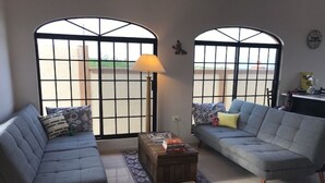 Un salón con dos sofás grises, una mesa de centro de madera y una lámpara. Hay cuencos para mascotas en el suelo.