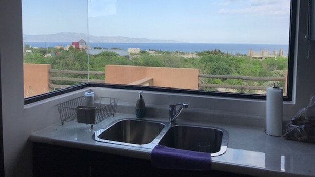 Cocina con un ventanal amplio que ofrece vista al mar y edificios a lo lejos.