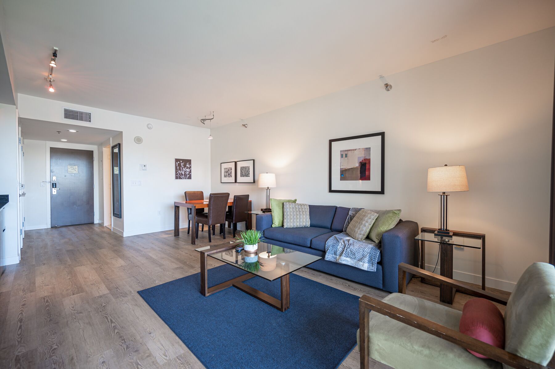 A modern living room with a blue sofa, a coffee table, and a dining area with chairs and a table.