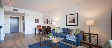 A modern living room with a blue sofa, a coffee table, and a dining area with chairs and a table.