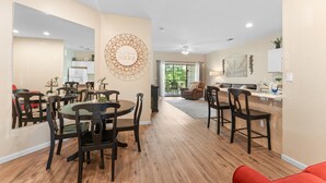 A spacious dining area with a large round table and multiple chairs, a kitchen area with modern appliances, and a view of the outdoors through a large window. - Golf View Resort Condo | No Stairs + Pools & Perks (Branson)