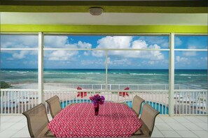 Un balcon avec une table et des chaises, un vase rempli de fleurs et une vue sur l’océan et la plage.