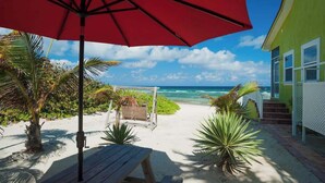 Een patio aan het strand met een rood parasol, een houten tafel en tropische planten.