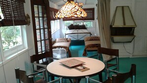 Une pièce confortable avec une table ronde, des chaises, un lit et une grande fenêtre avec des stores.