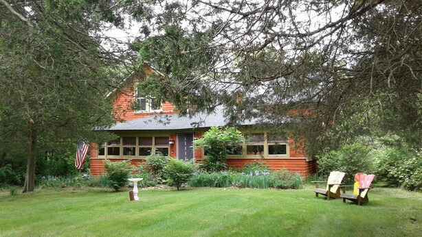 Un chalet rustique doté d’un toit en pente, entouré d’une pelouse bien entretenue et d’arbres denses.