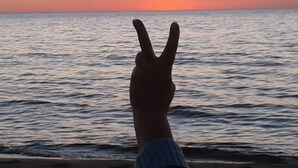 Une main faisant le signe de la paix sur fond de coucher de soleil sur l’océan.