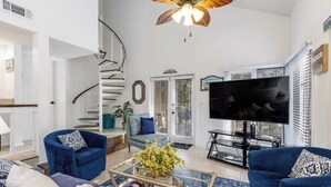 Un salon moderne doté d’un escalier en colimaçon, d’un téléviseur à écran plat et d’une grande fenêtre avec des stores.