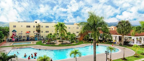 A swimming pool surrounded by palm trees and a playground, with a building in the background.