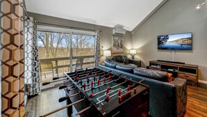 A modern living room with a foosball table, a sofa, a TV, and a large window offering a scenic view. - Camelback,Aquatopia/Camelbeach Waterparks,Pool,Tennis,Paintball,Jacuzzi,Zip-Line (Tannersville)