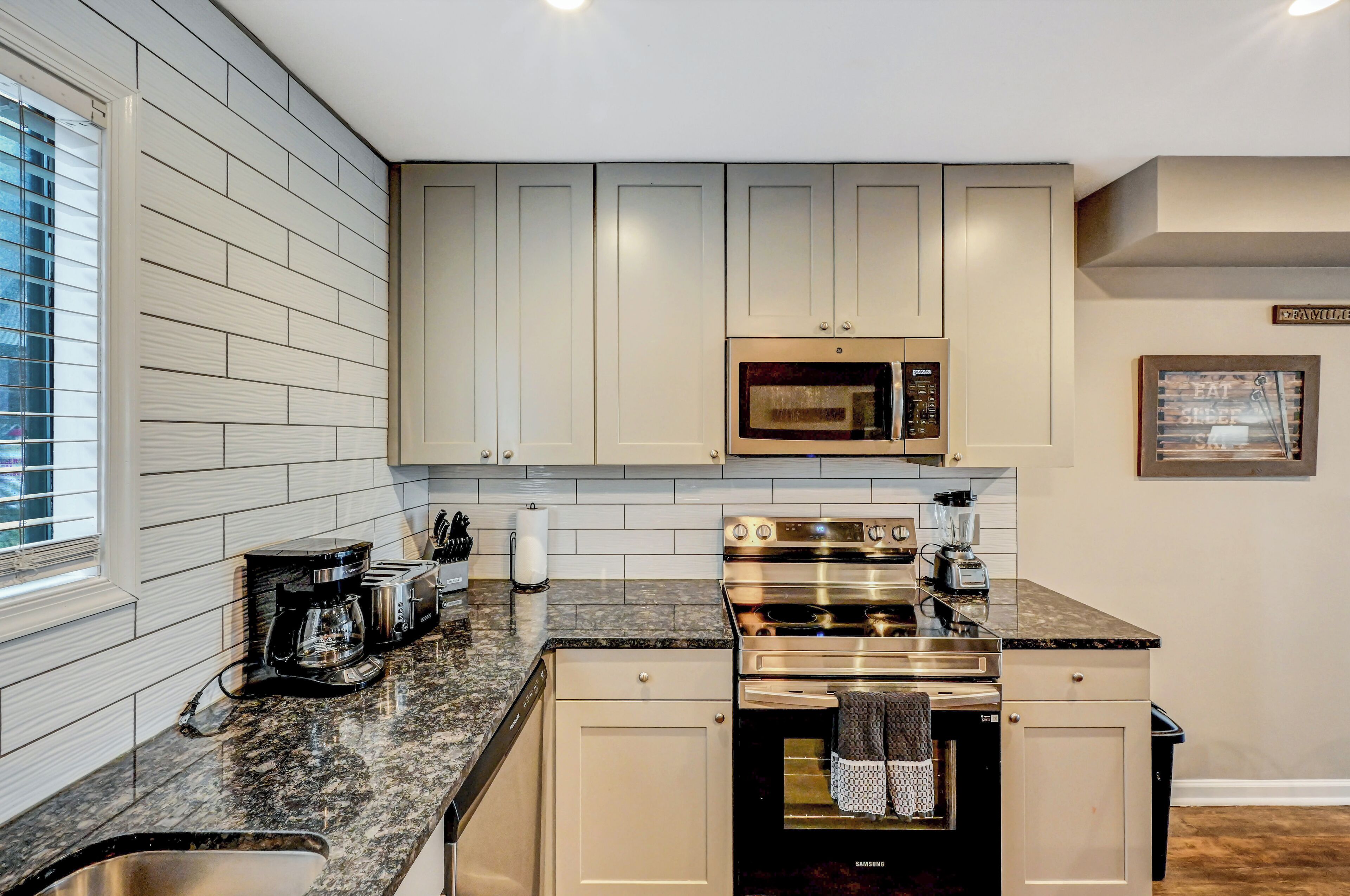 A modern kitchen with white cabinets, a stainless steel oven, a microwave, and a granite countertop.