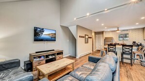 A modern living room with a sofa, coffee table, and TV. A kitchen with a dining area is visible in the background. - Camelback,Aquatopia/Camelbeach Waterparks,Pool,Tennis,Paintball,Jacuzzi,Zip-Line (Tannersville)