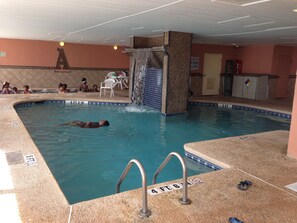 An indoor swimming pool with a waterfall feature, a diving board, and a sign indicating shallow water. - Gorgeous Direct Oceanfront 2-BR Condo In The 2nd Floor in Broadwalk, Downtown MB (Myrtle Beach)