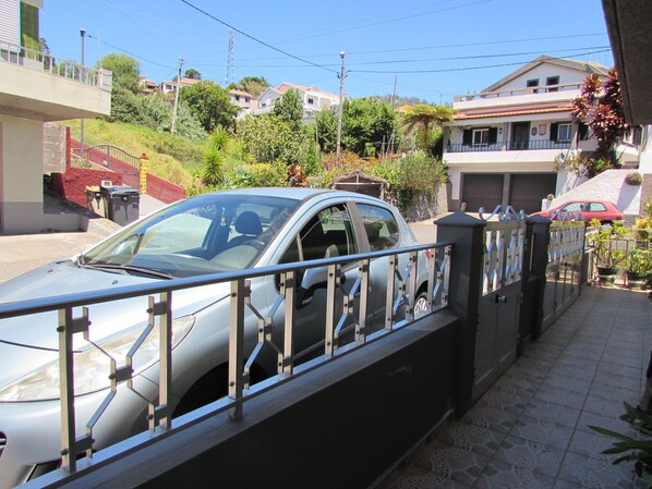 Zona residenziale con viale recintato, un'auto parcheggiata e case sullo sfondo.