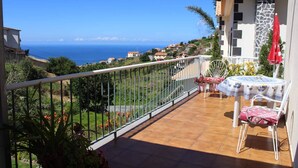 Un balcon avec vue sur la mer, une table avec des chaises et un parasol rouge.
