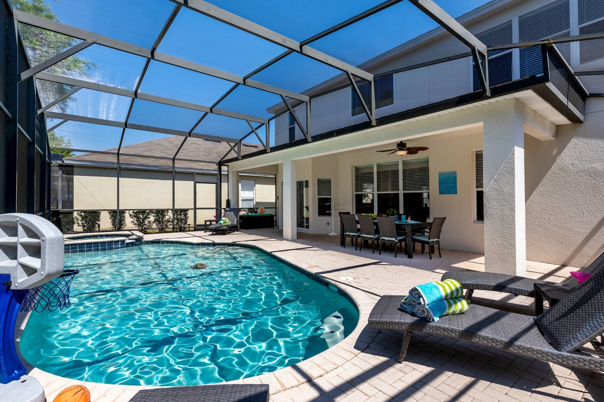 A covered outdoor swimming pool area with a patio, lounge chairs, and a dining table.