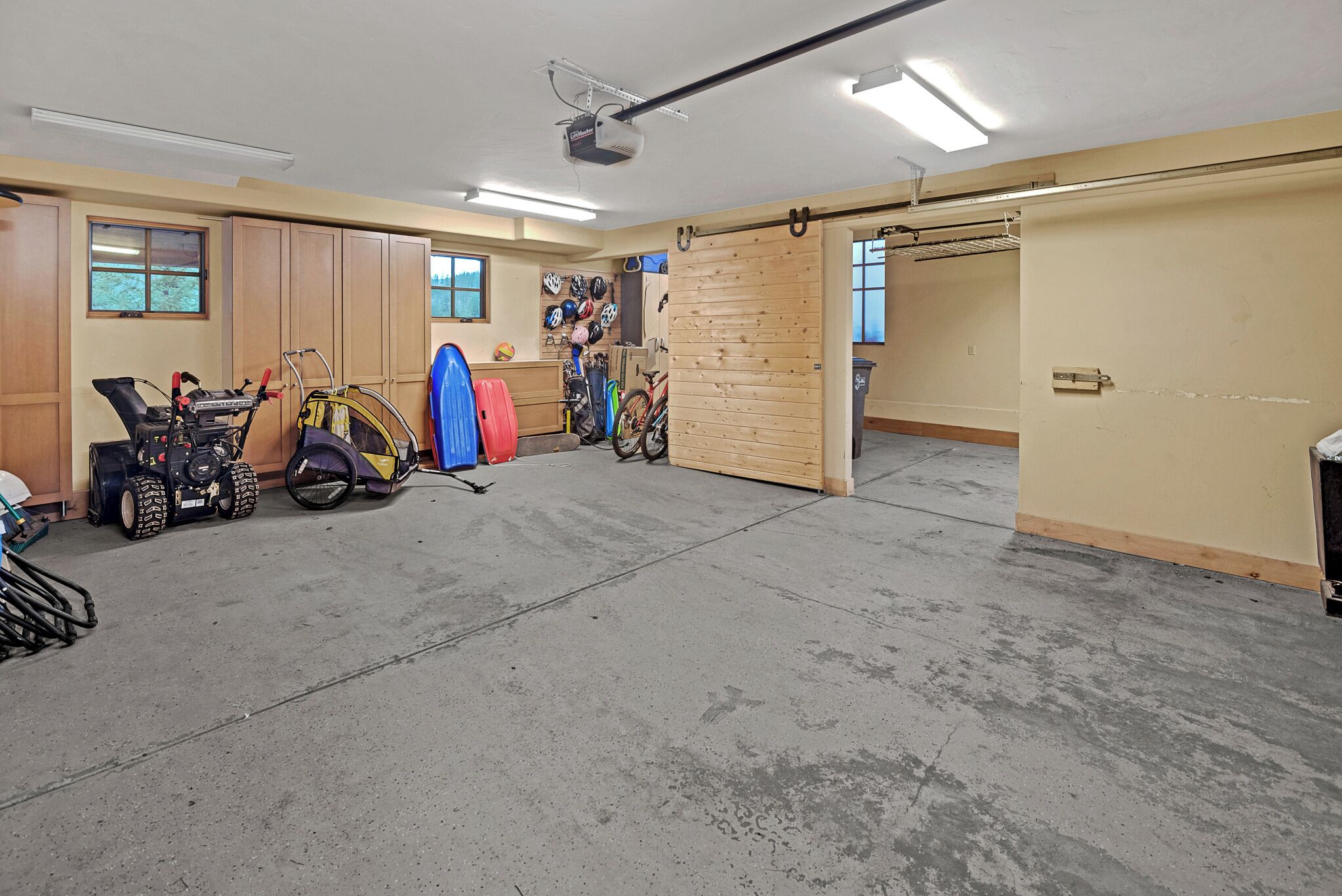 A garage with a concrete floor, wooden cabinets, a bicycle, and a surfboard.