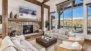 Una sala de estar acogedora con chimenea de piedra, un ventanal con vistas a la montaña y un área de descanso confortable.