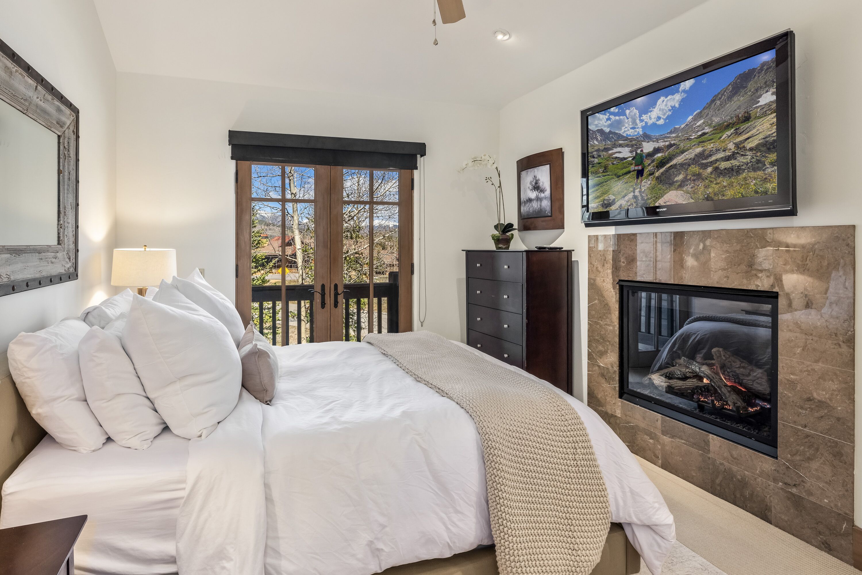 Ein Schlafzimmer mit Bett, Kamin, Fernseher und Blick ins Freie.