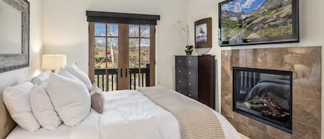 Ein Schlafzimmer mit Bett, Kamin, Fernseher und Blick ins Freie.