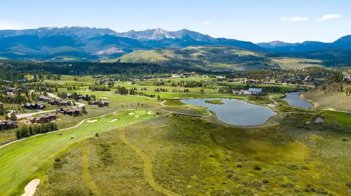 Um campo de golfe com vários lagos e montanhas ao fundo.