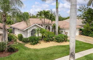 A residential property with a well-maintained lawn, palm trees, and a house with a tiled roof and arched windows.